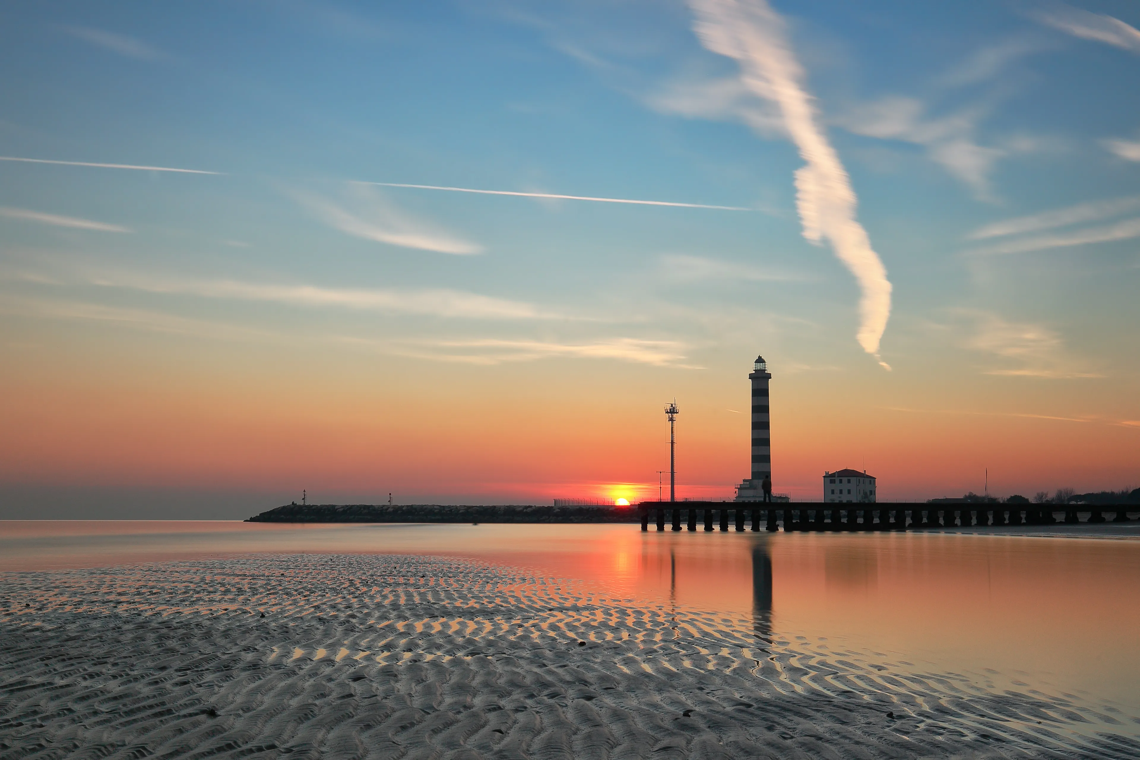 Sunset at the lighthouse on the beach, with the reflection in the low tide, Jesolo, Veneto, Italy