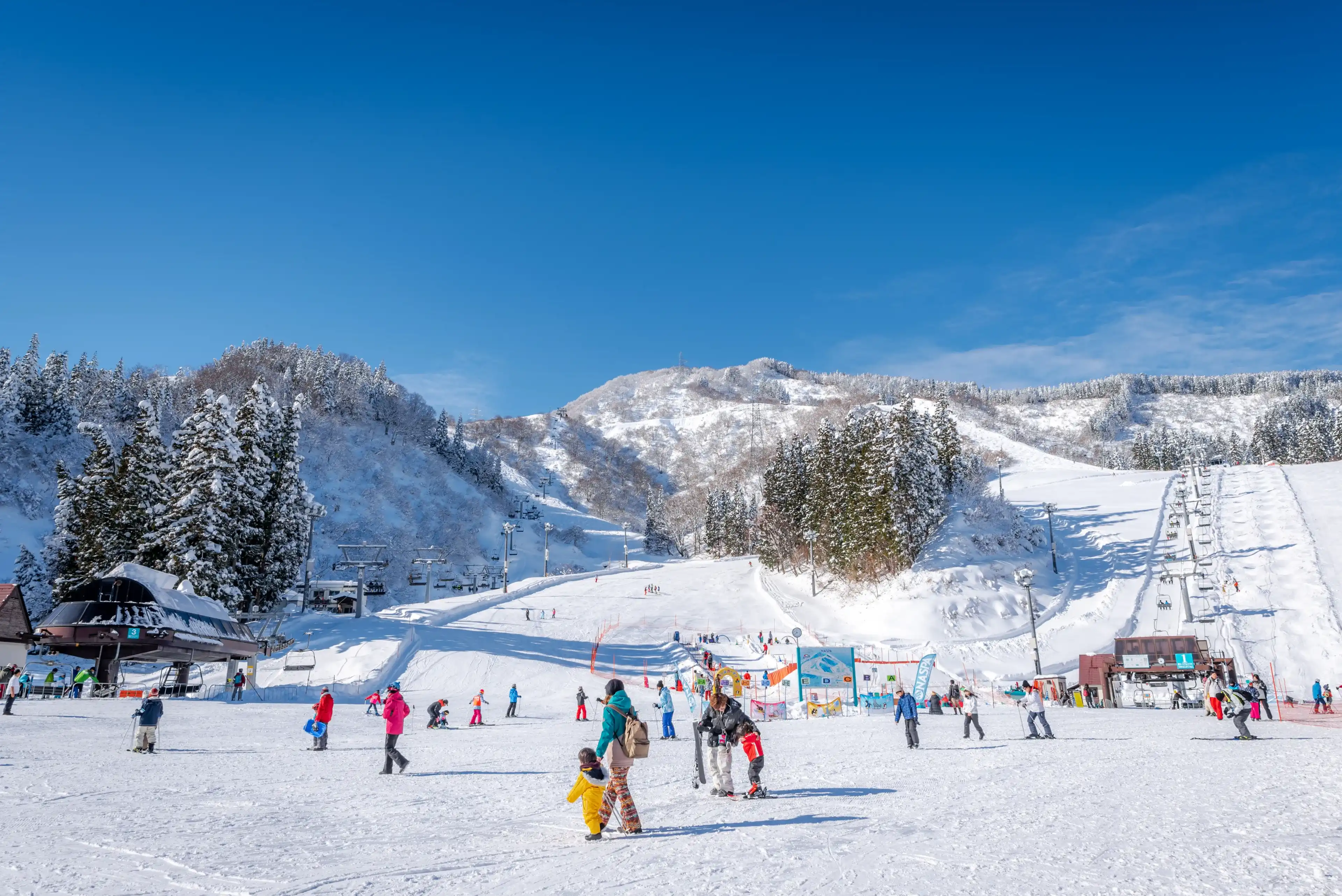 Minamiuonuma, Niigata, Japan, January 03, 2019 : People walking and skiing with mountains view in the background at NASPA Ski Garden in Yuzawa City. Minamiuonuma, Niigata, Japan, January 03, 2019 : People walking and skiing with mountains view in the background at NASPA Ski Garden in Yuzawa City.