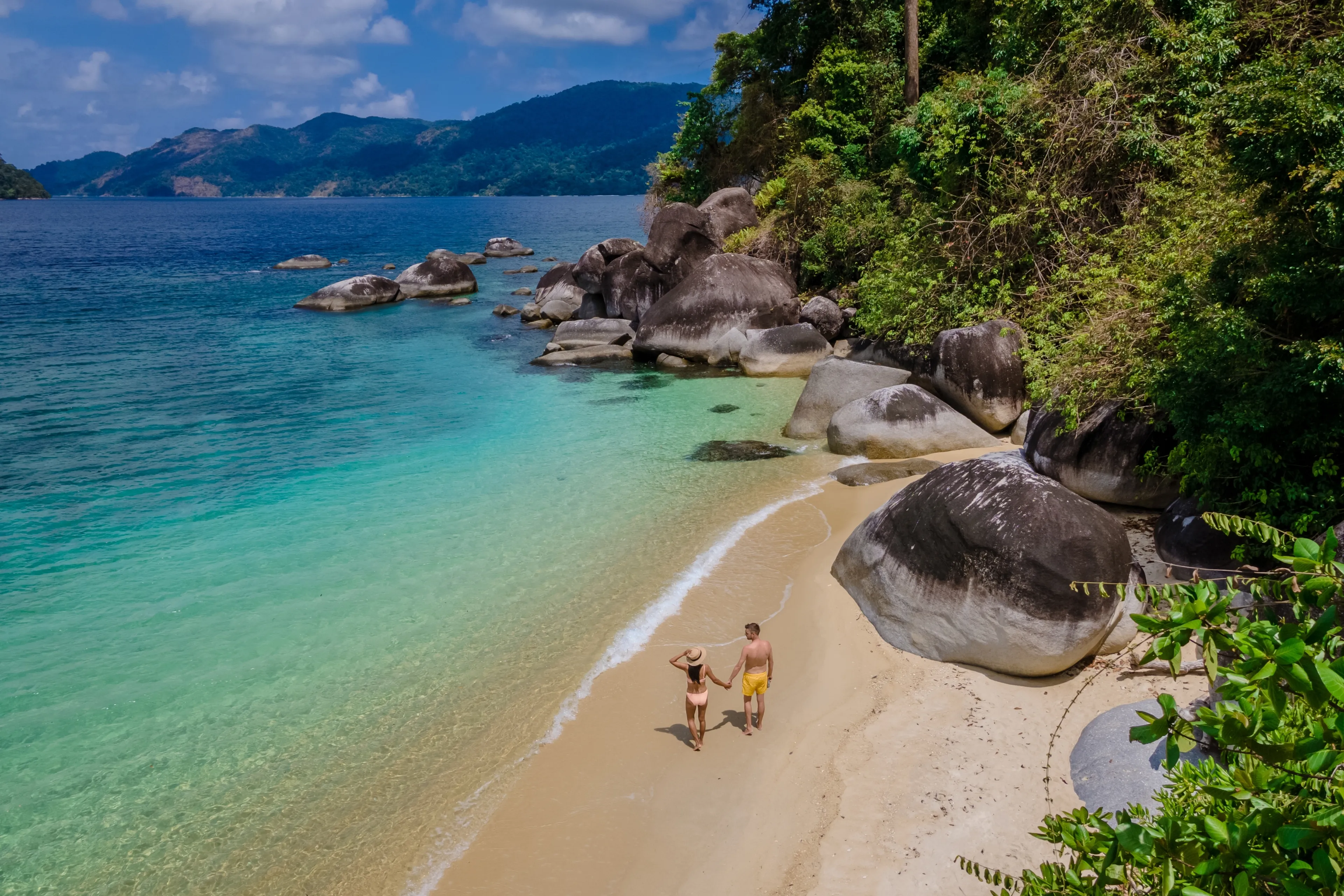couple of men and woman on the beach of Ko Adang Island in front of Koh Lipe Island Southern Thailand with turqouse colored ocean and white sandy beach, drone view from above