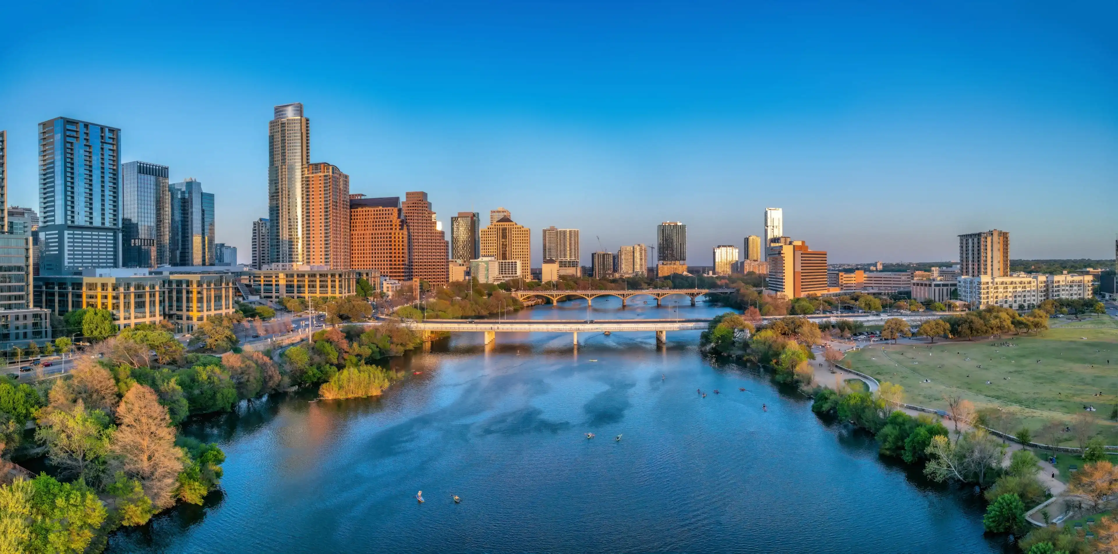 Colorado River near the district urban area of Austin, Texas. There are bridges over the river and a view of skyscraper buildings on the left and large field at the right side against the sunset sky. Colorado River near the district urban area of Austin, Texas. There are bridges over the river and a view of skyscraper buildings on the left and large field at the right side against the sunset sky.
