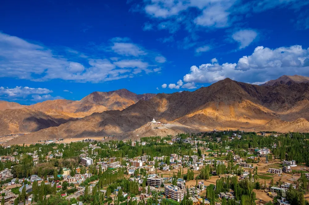 Leh, Ladakh India - 07 26 2024: A vibrant view of Leh, Ladakh, showcasing a leh city with shanti stupa, blend of lush greenery and arid mountains under a bright blue sky with scattered clouds.