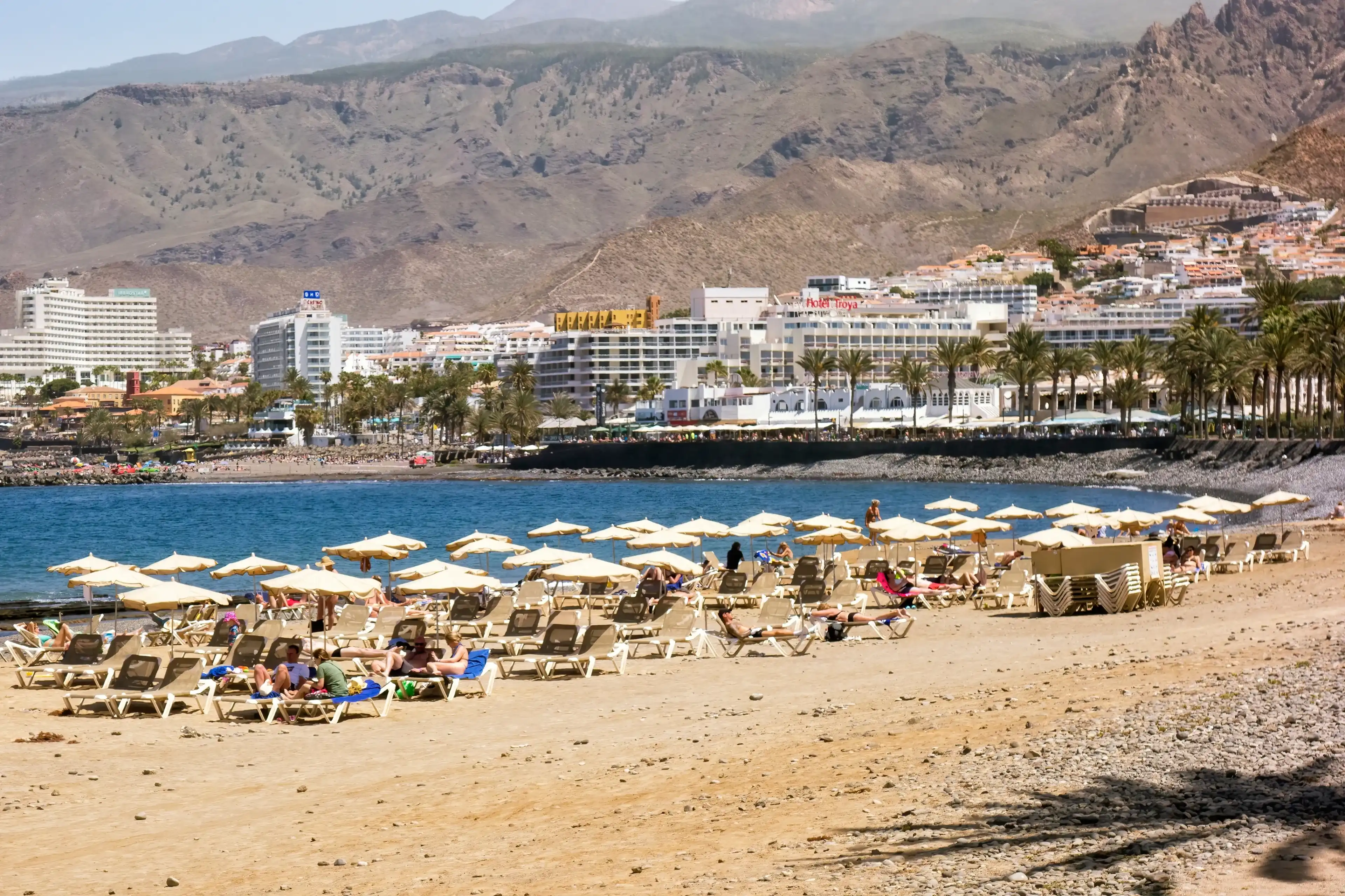 Arona, Tenerife, Spain; 04-23-2024: Playa de las Vistas in the Tenerife city of Arona with people sunbathing and with umbrellas and views of the Atlantic Sea and the landscape of the island Arona, Tenerife, Spain; 04-23-2024: Playa de las Vistas in the Tenerife city of Arona with people sunbathing and with umbrellas and views of the Atlantic Sea and the landscape of the island