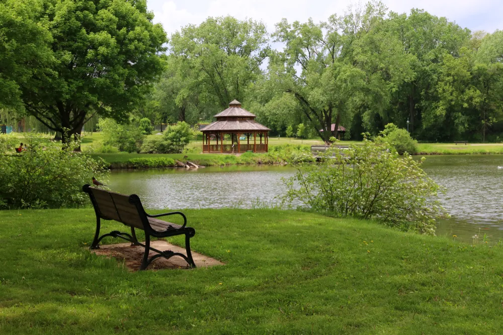Midwest nature background with city park view.Beautiful late spring landscape with bench in a foreground, trees around the pond and wooden gazebo in a city park.Lakeview park, Middleton, Madison area.