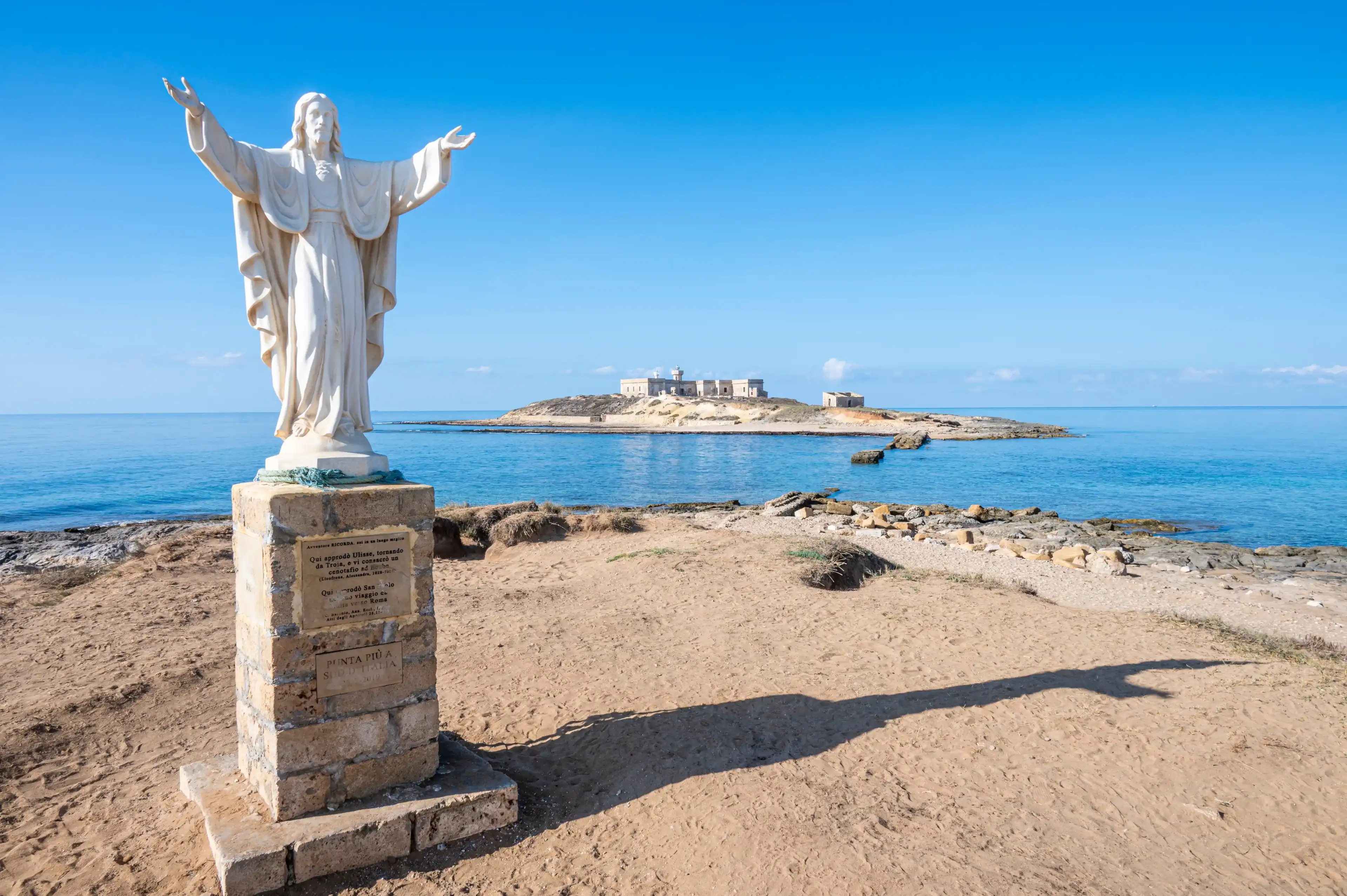 Portopalo, Italy - 09-14-2022: The statue of Christ Redeemer in Portopalo with the Island of Correnti in background Portopalo, Italy - 09-14-2022: The statue of Christ Redeemer in Portopalo with the Island of Correnti in background