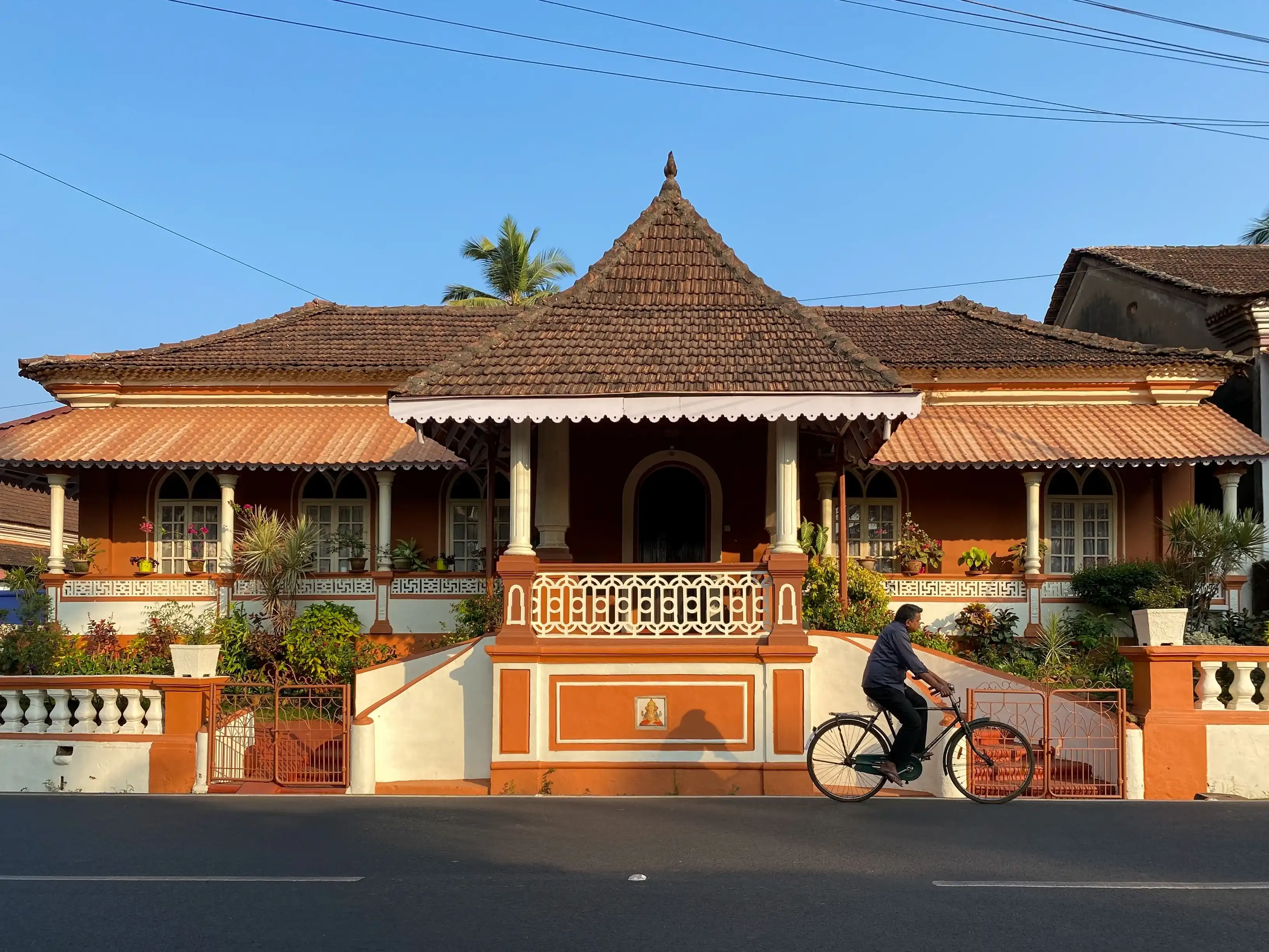 Margao, India - January 21 2023: A man riding a bicycle past a beautiful old house with traditional architecture in South Goa. Margao, India - January 21 2023: A man riding a bicycle past a beautiful old house with traditional architecture in South Goa.
