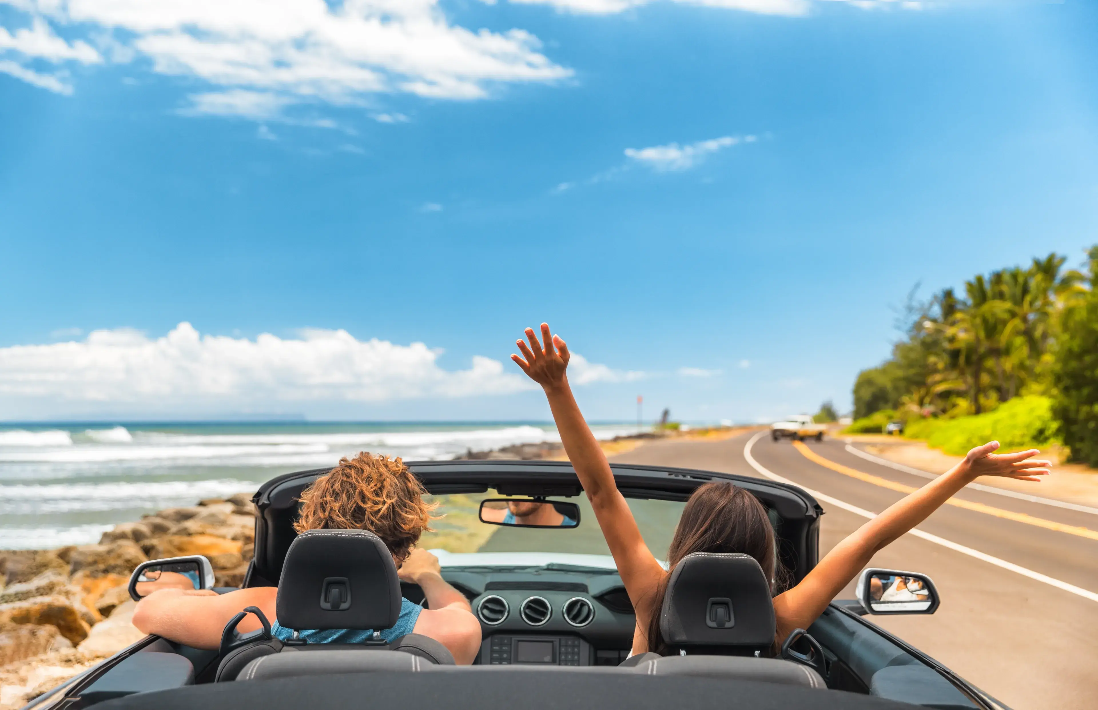 Road trip car holiday happy couple driving convertible car on summer travel Hawaii vacation. Woman with arms up having fun, young man driver Road trip car holiday happy couple driving convertible car on summer travel Hawaii vacation. Woman with arms up having fun, young man driver