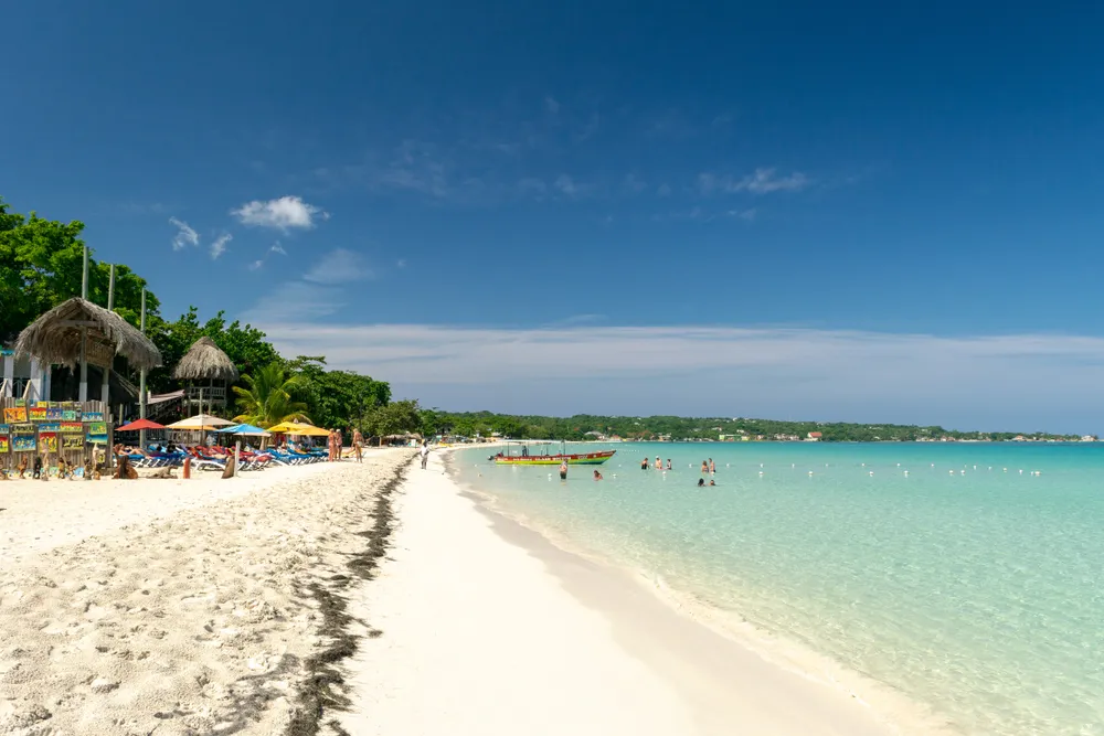 Negril, Jamaica - May 30 2015: People/ tourists at Seven Mile Beach on Westmoreland coast on sunny summer vacation day. Beautiful tropical Caribbean island holiday scene. Rasta color glass bottom boat