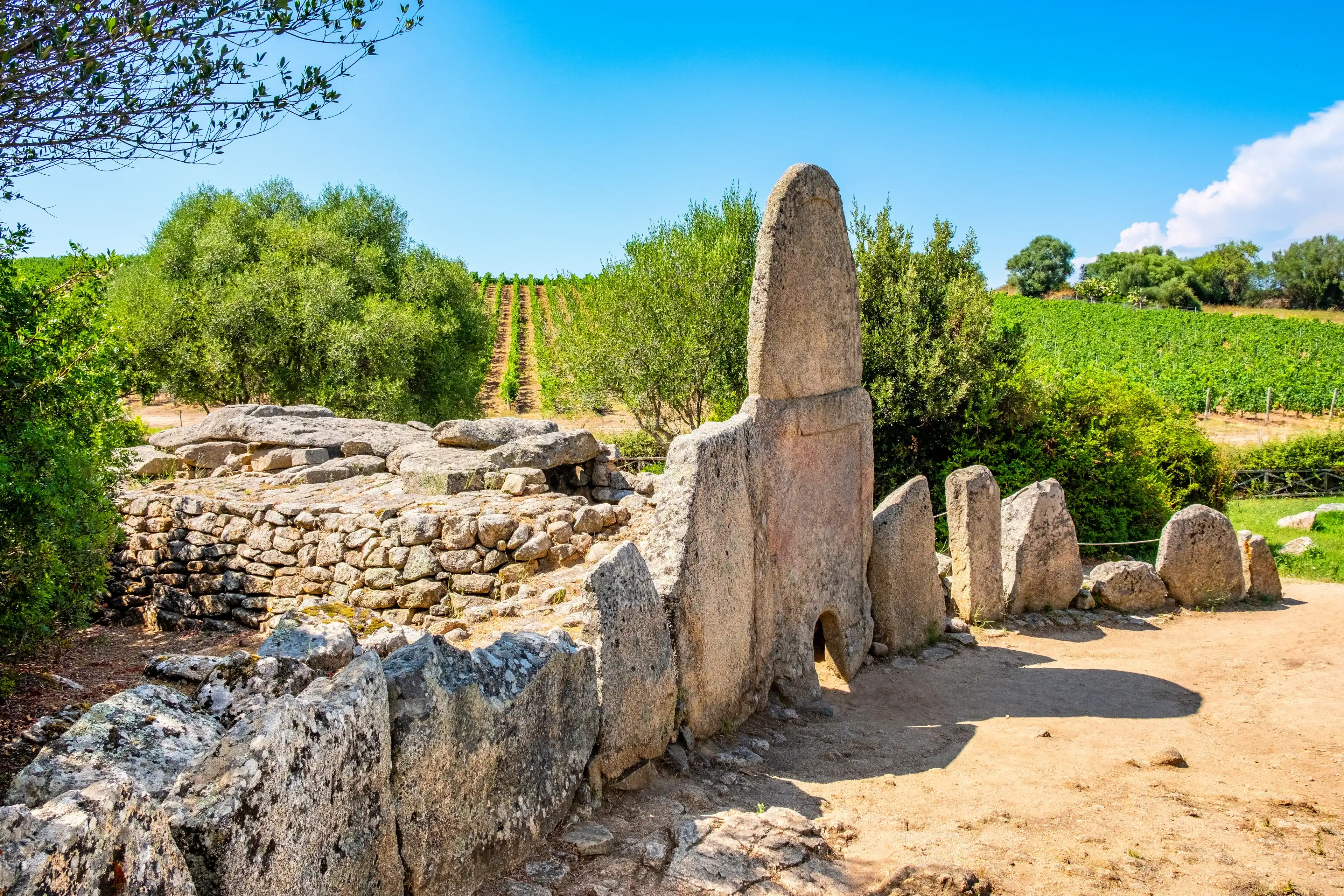 Arzachena, Sardinia / Italy - 2019/07/19: Archeological ruins of Nuragic necropolis Giants Tomb of Coddu Vecchiu - Tomba di Giganti Coddu Vecchiu - with front grave stones of Neolithic cemetery Arzachena, Sardinia / Italy - 2019/07/19: Archeological ruins of Nuragic necropolis Giants Tomb of Coddu Vecchiu - Tomba di Giganti Coddu Vecchiu - with front grave stones of Neolithic cemetery