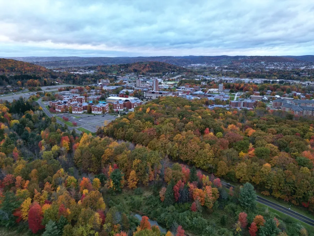 arial view of binghamton university in vestal, new york during autumn with fall foliage (leaves changing colors) at dusk, sunset, cloudy sky (library tower, student union, mountainview residence hall)