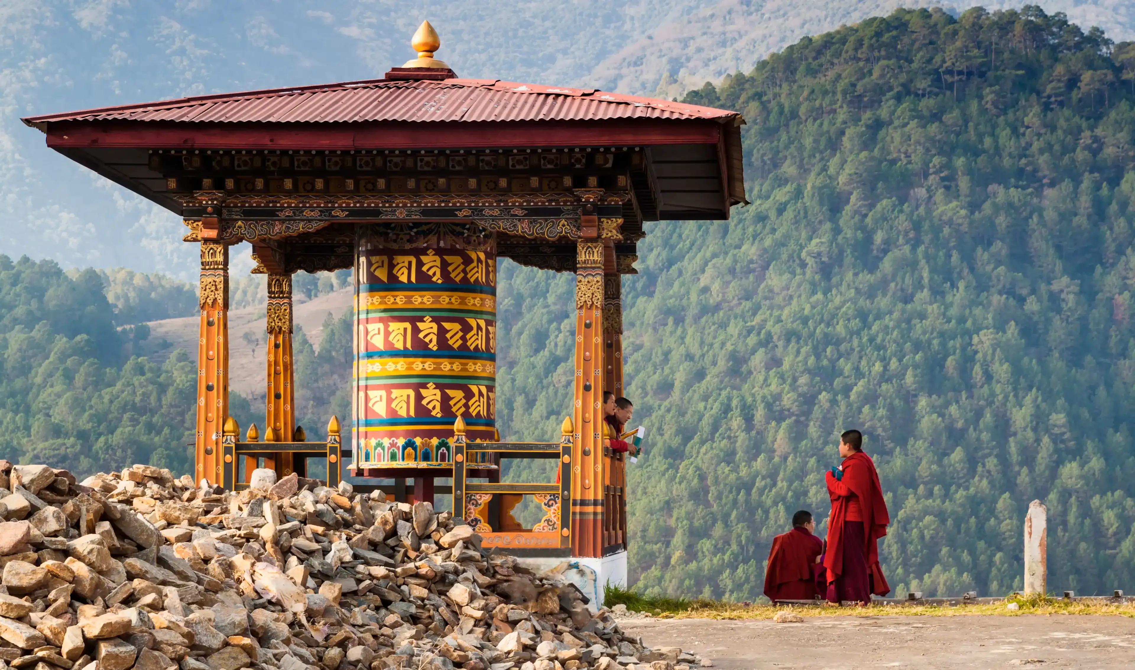 Punakha/Bhutan - March 1, 2016: young women monks of the Buddhist monastery in their traditional red robes before classes next to the prayer wheel against the background of the Himalayan mountains Punakha/Bhutan - March 1, 2016: young women monks of the Buddhist monastery in their traditional red robes before classes next to the prayer wheel against the background of the Himalayan mountains