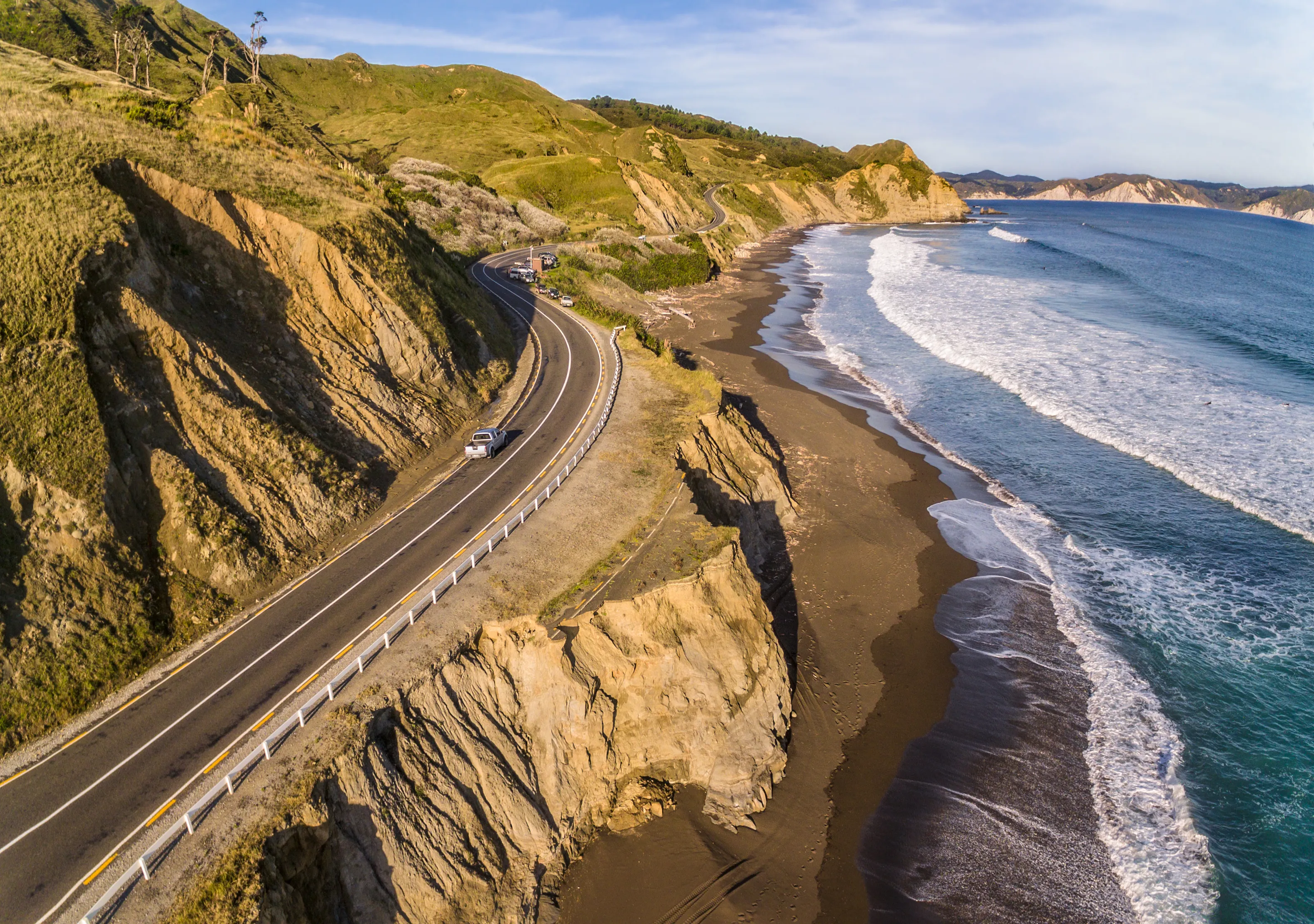 Aerial view of the road leading to Mahia peninsula around ocean. New road next to old damaged asphalt road. Golden hour. North Island of New Zealand.