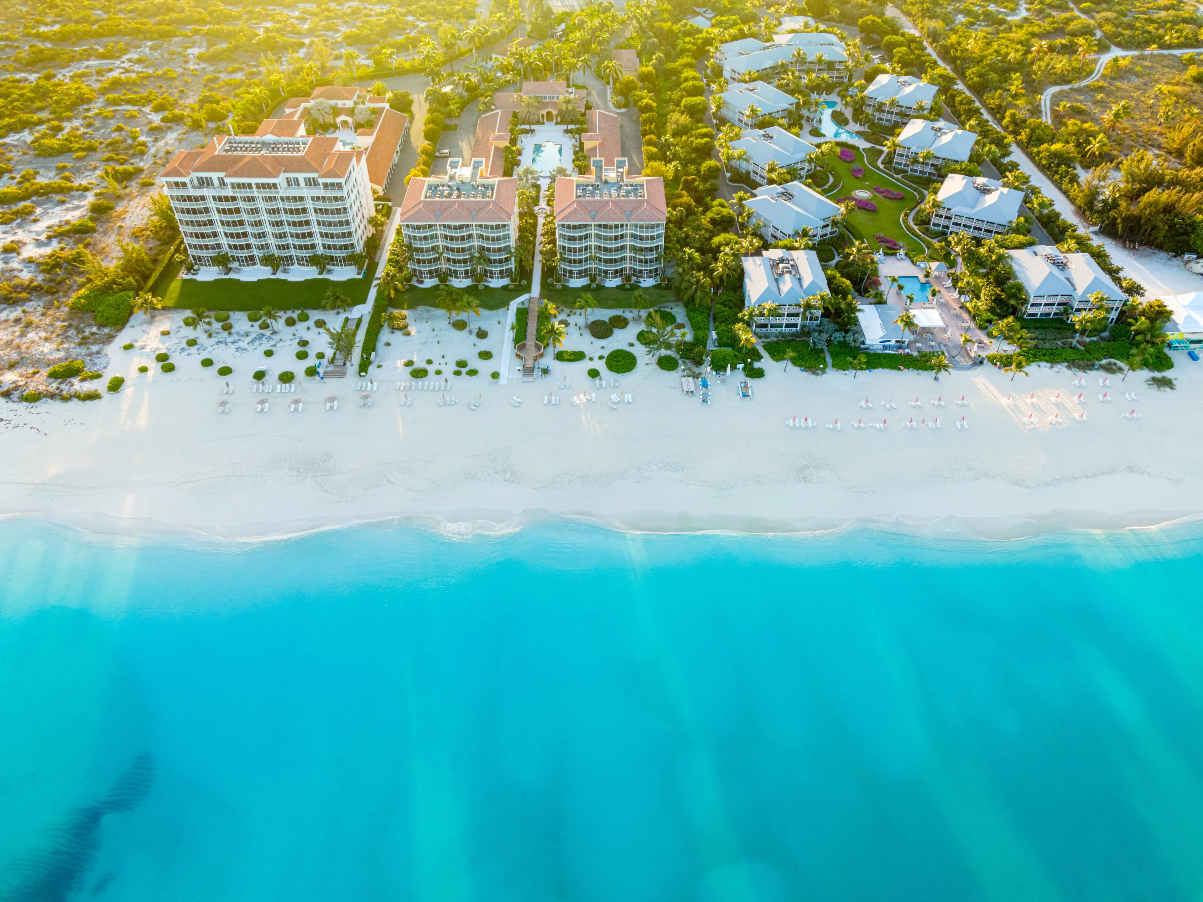 Grace Bay, Turks and Caicos - February 20 2021: Golden sunrise bursts over a stretch of land and resorts along Grace Bay Beach with its white sandy shore and blue waves in foreground