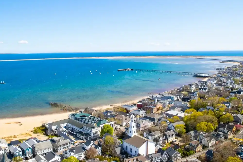 Provincetown, Massachusetts, United States - May 3th, 2023 : View of the harbour located next to the buildings of Provincetown. There is a blue sky. A sandy beach is located along the shore. Provincetown, Massachusetts, United States - May 3th, 2023 : View of the harbour located next to the buildings of Provincetown. There is a blue sky. A sandy beach is located along the shore.