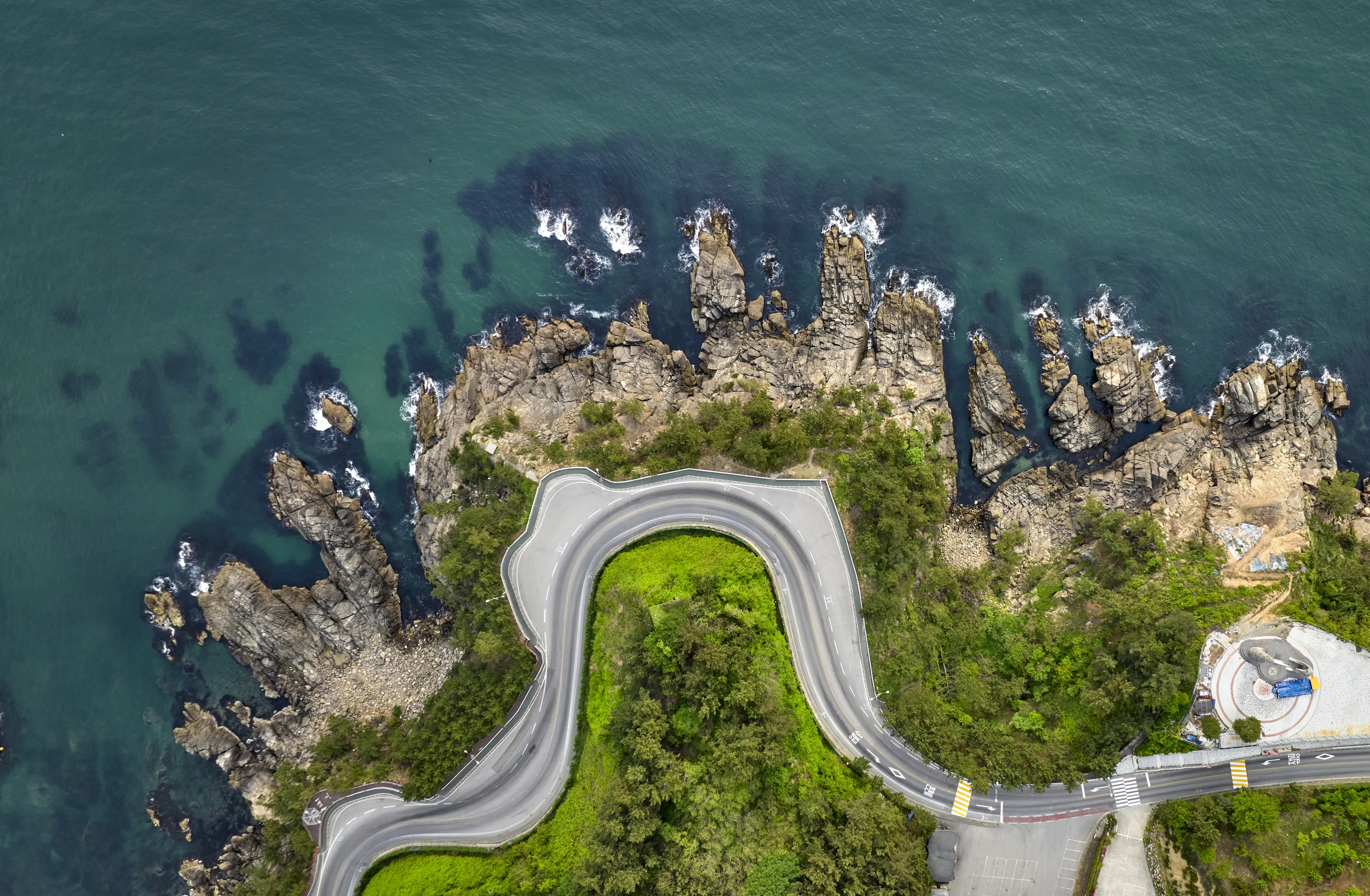 Aerial and top angle view of curved road with Tower of Hope besides rocks and sea at Gyo-dong of Samcheok-si, South Korea 