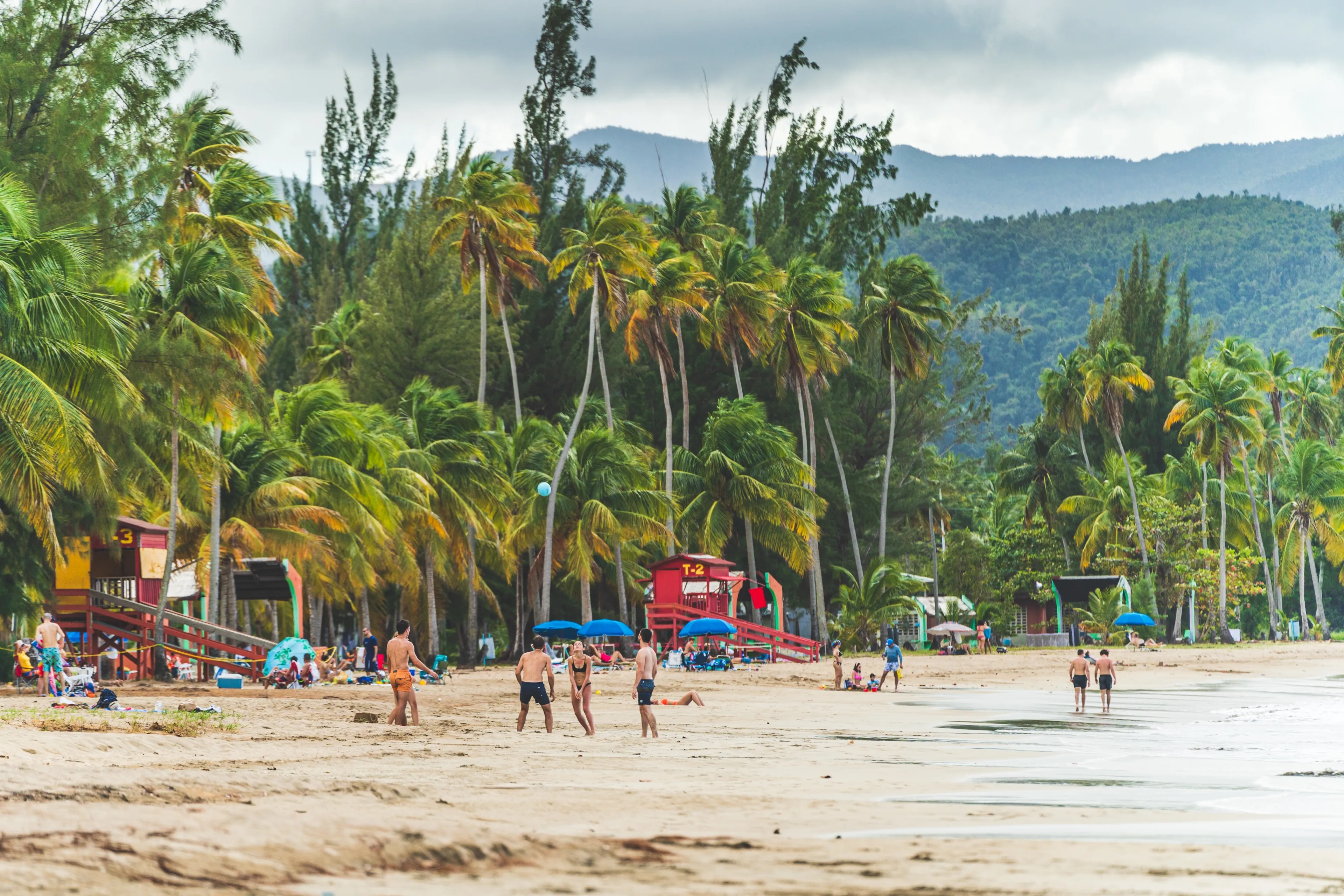 Luquillo, Puerto Rico - February 11 2021: People enjoying activities at Luquillo beach in Puerto Rico against tropical background of Luquillo mountains and green palm trees. Wide High quality photo